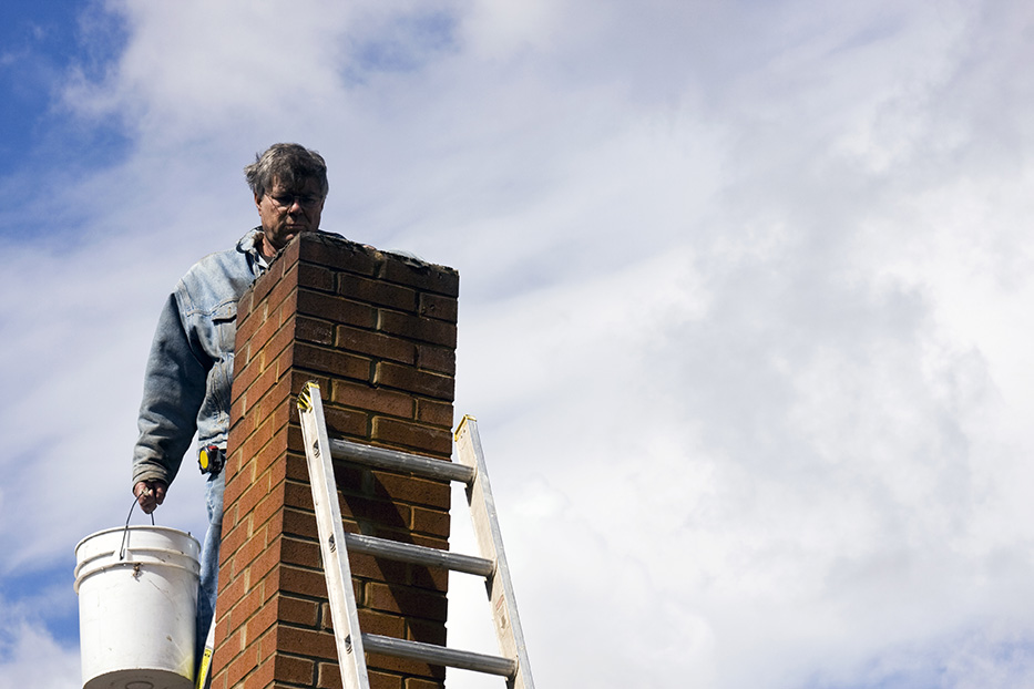 mason on a ladder repairing a damaged chimney