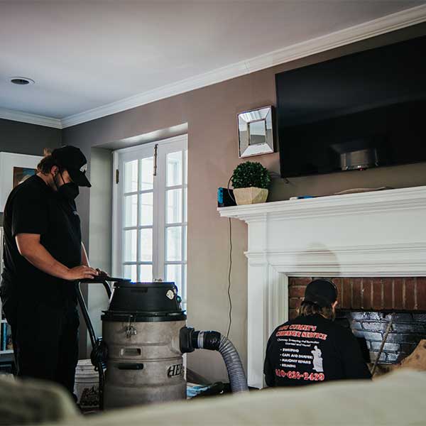 Two Techs sweeping a chimney with a white mantel and TV sitting on top with double doors to the left.