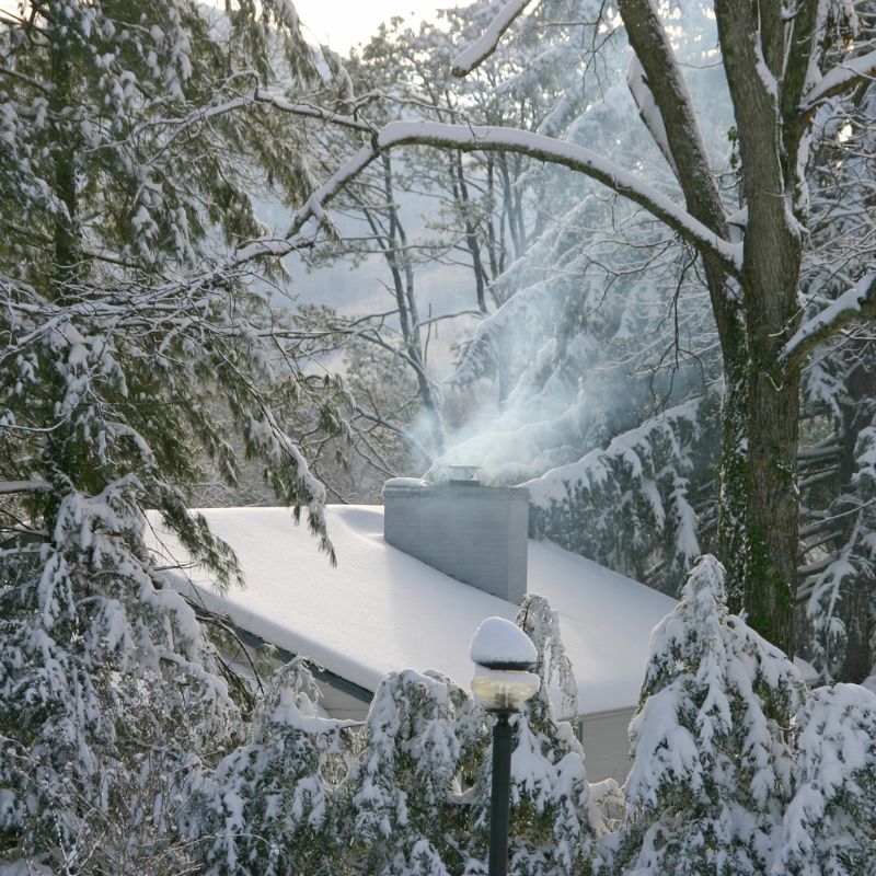 a snow-covered roof with a smoking chimney in a snow-covered forest
