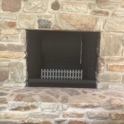 Stone fireplace with black interior, metal grate, and hanging chain